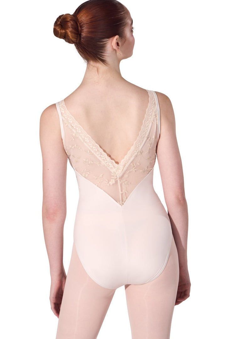 A woman modeling a light beige or nude-colored leotard from the back, showing a lace-trimmed open back and smooth fabric below, against a plain white background.