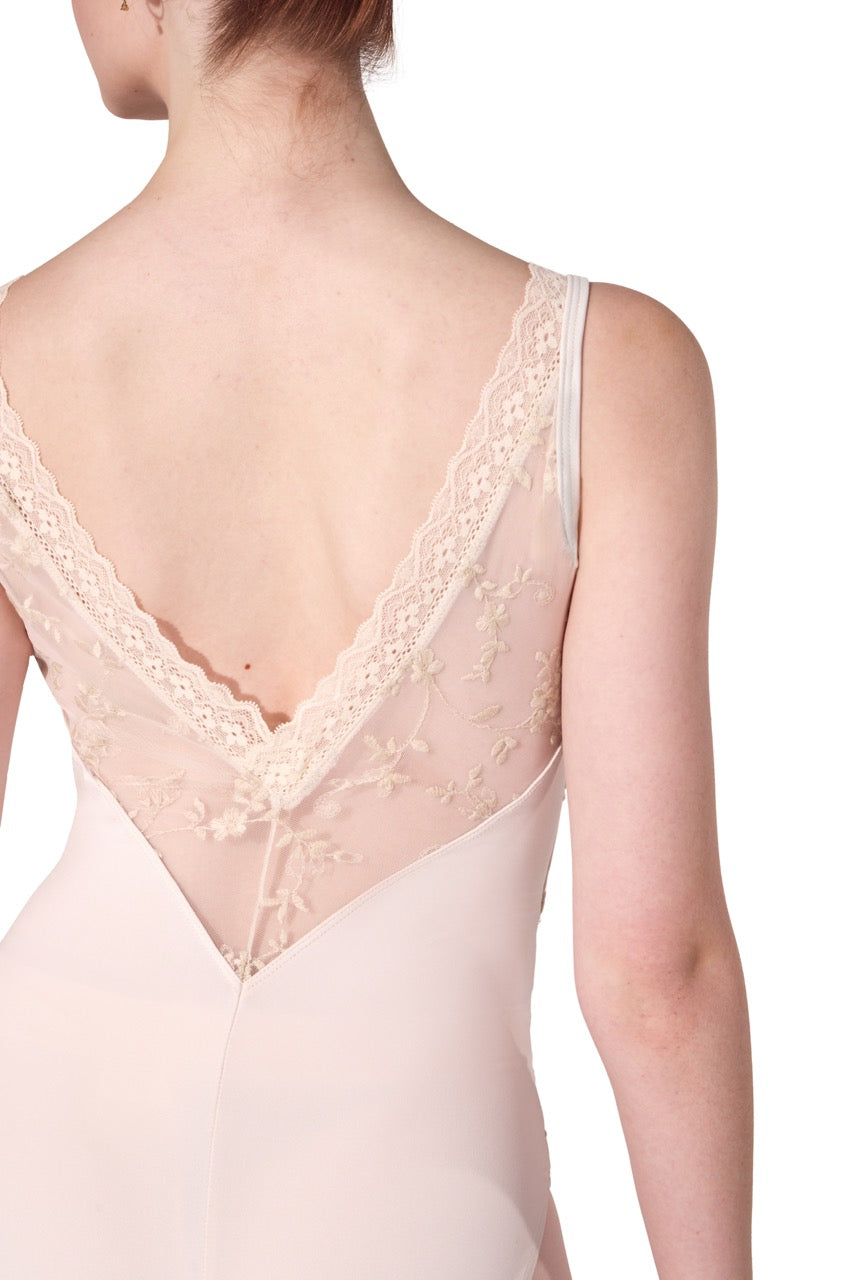Close-up back view of a model wearing a pale blush pink slip or lingerie dress with a deep V-neck and delicate floral lace trim.