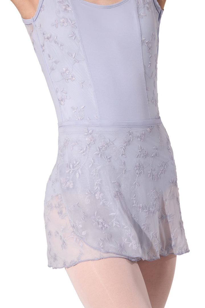 A sleeveless lavender dance leotard with a sheer floral embroidered overlay skirt, shown on a model against a white background.