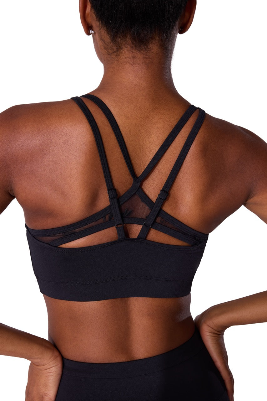 Rear view of a woman wearing a black sports bra with multiple crisscrossing strappy details on the back, set against a plain white background.