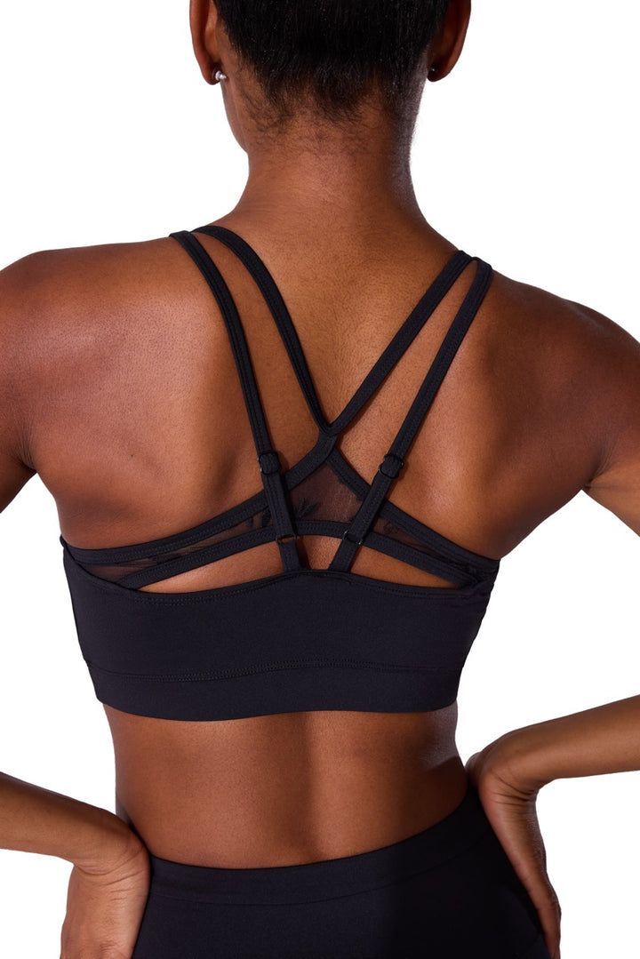 Rear view of a woman wearing a black sports bra with multiple crisscrossing strappy details on the back, set against a plain white background.
