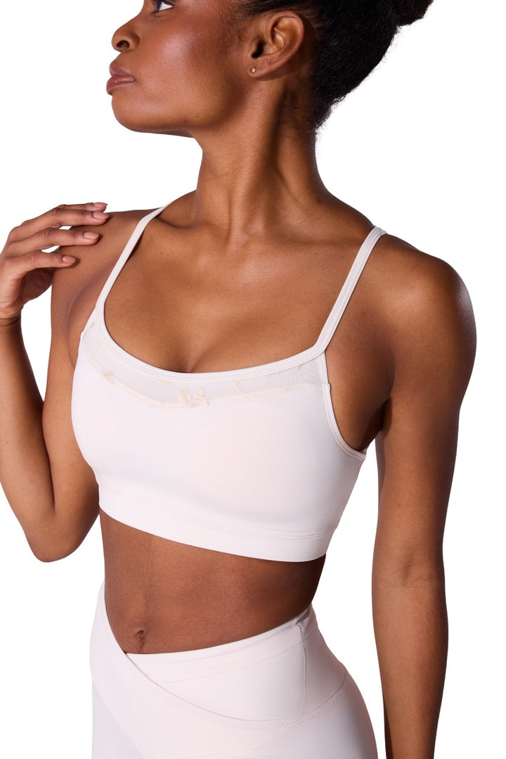 A woman wearing a white scoop-neck sports bra and matching high-waisted leggings, shown from the side against a plain white background.
