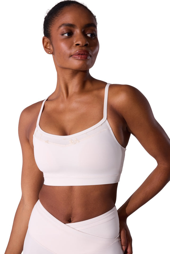 A woman modeling a white sports bra and matching white wrap-style bottoms against a plain white studio background.