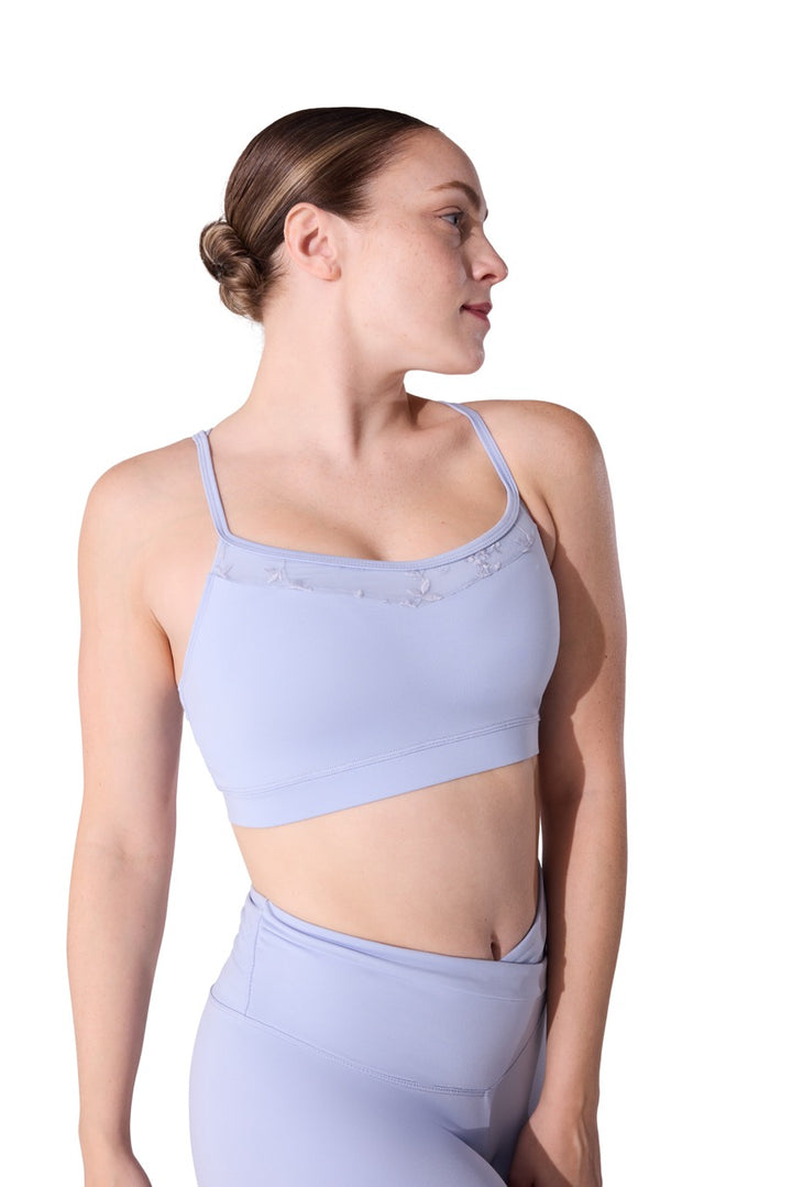 A woman in profile wearing a light periwinkle blue sports bra and matching high-waisted leggings against a solid white background.
