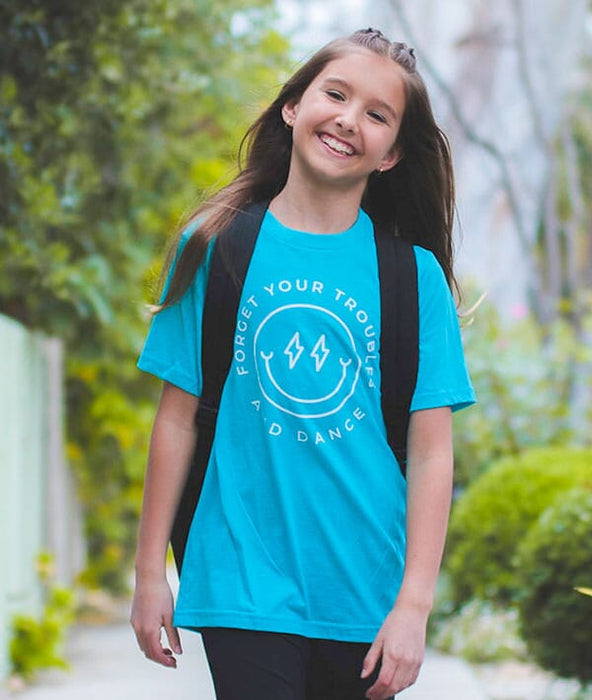 Young girl wearing a blue t-shirt with a logo and text, standing outdoors.