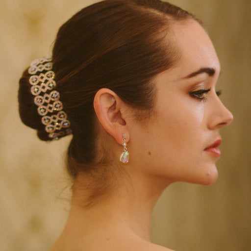 Woman with elegant hair bun and earrings against a neutral background
