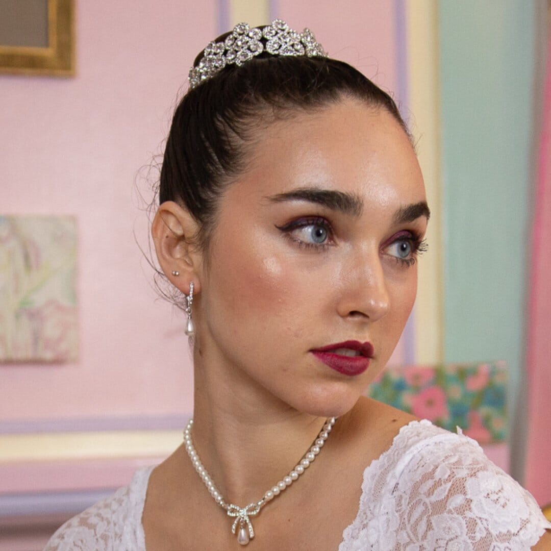 Woman wearing a tiara and pearl necklace in a pastel-colored room