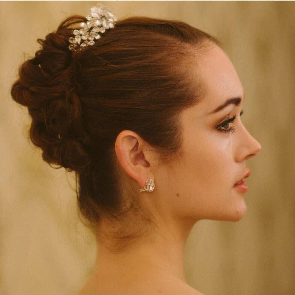 Woman with elegant hair bun and jewelry against a neutral background
