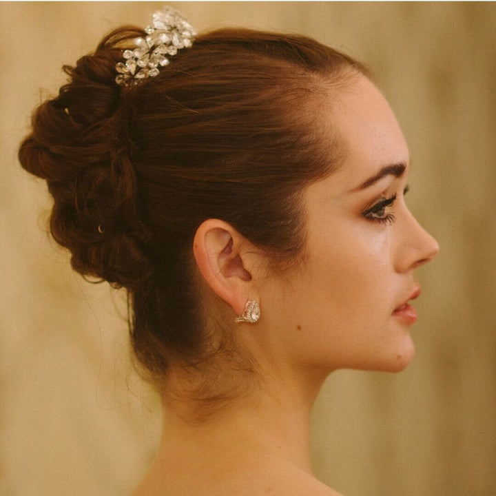 Woman with elegant hair bun and jewelry against a neutral background
