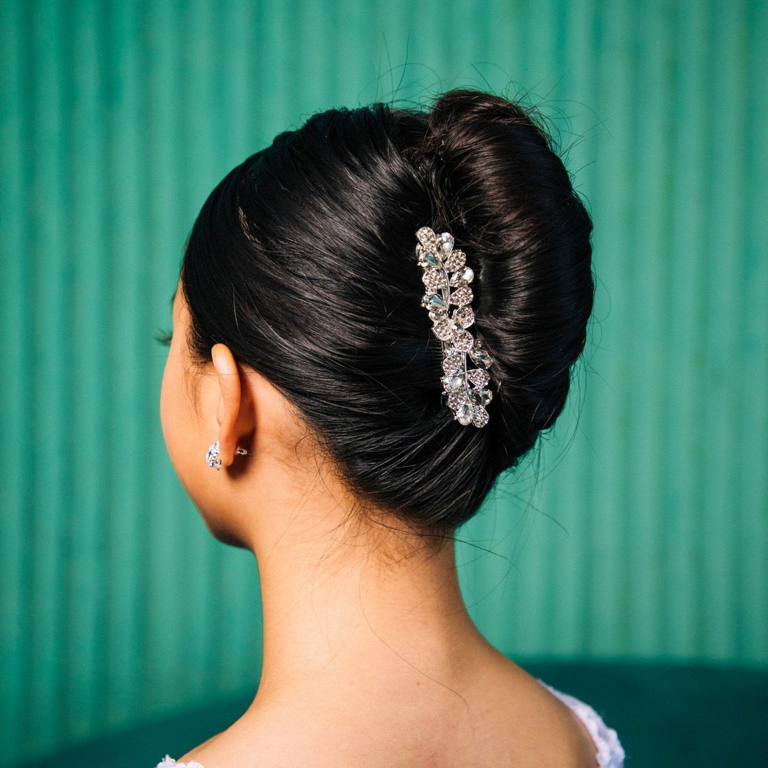 Woman with elegant hair bun adorned with a decorative hairpiece against a teal background
