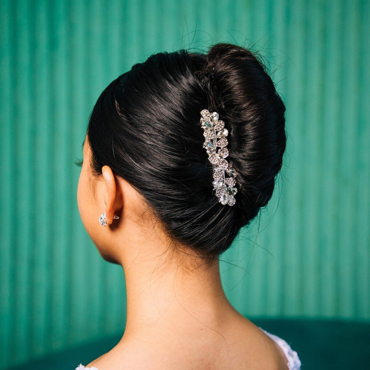 Woman with elegant hair bun adorned with a decorative hairpiece against a teal background