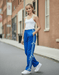 Woman wearing a white tank top and blue pants with white drawstrings on a street.