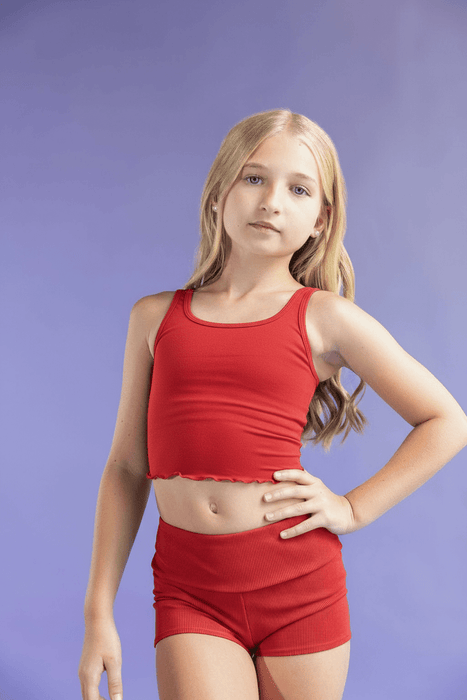 Young girl wearing a red tank top and shorts against a purple background