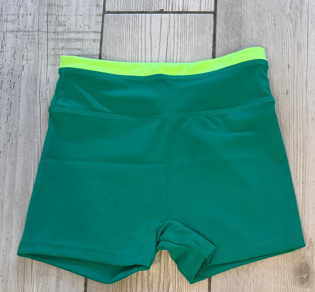 Three pairs of shorts in pink, green, and black on a wooden floor.