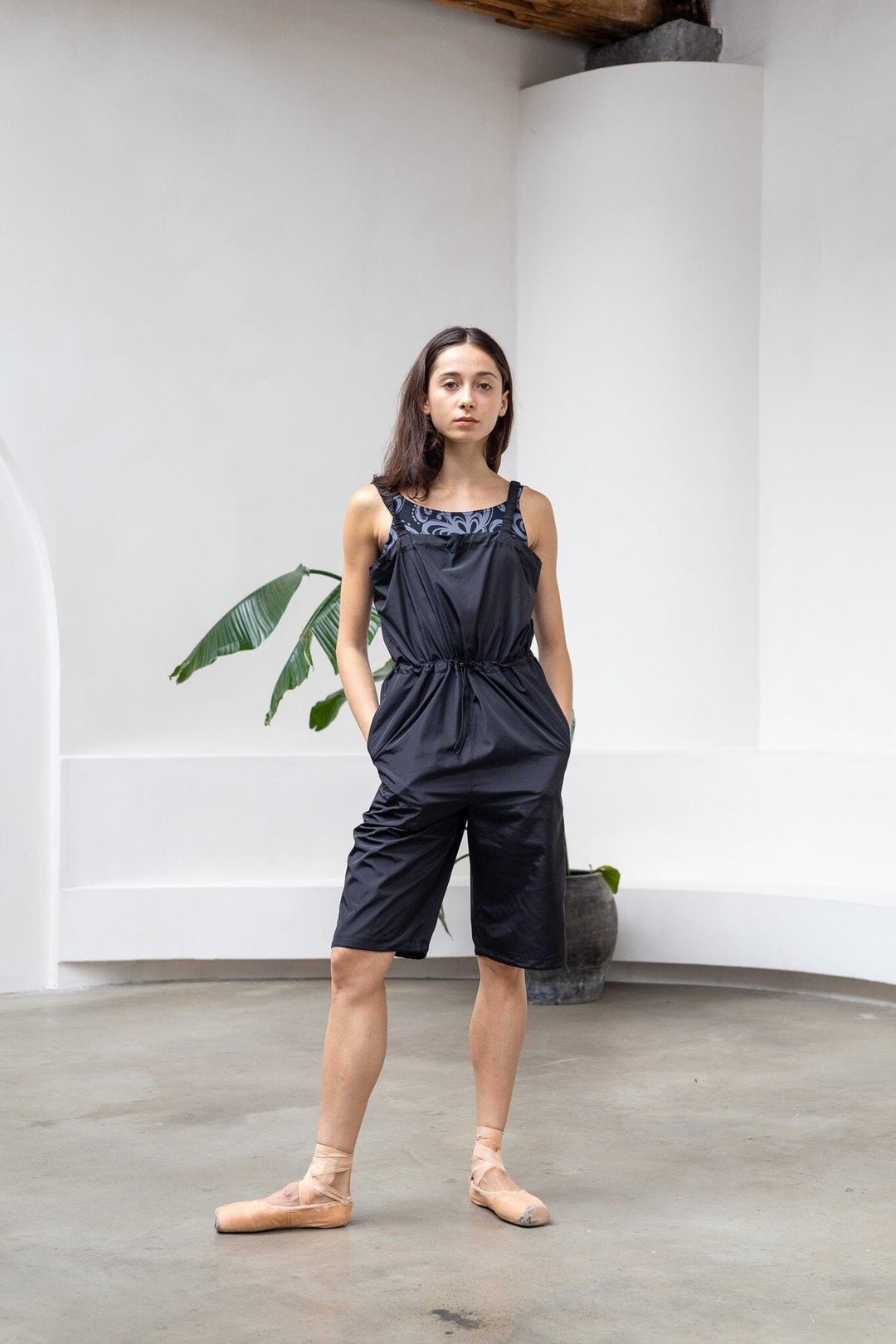 Woman wearing a black romper standing in a minimal indoor setting.