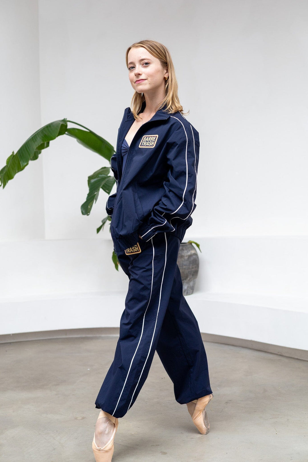 Woman wearing a navy tracksuit with white piping in a minimalistic room.