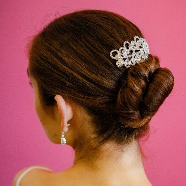 Woman with a styled hair bun wearing a decorative hair clip against a pink background