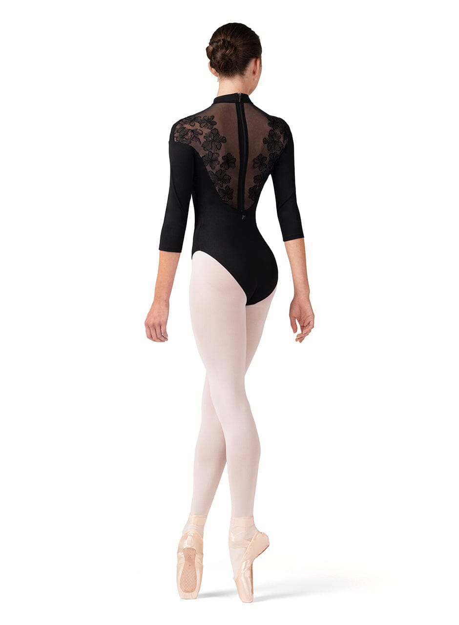 Ballerina wearing a black leotard with floral lace details and white tights on a white background