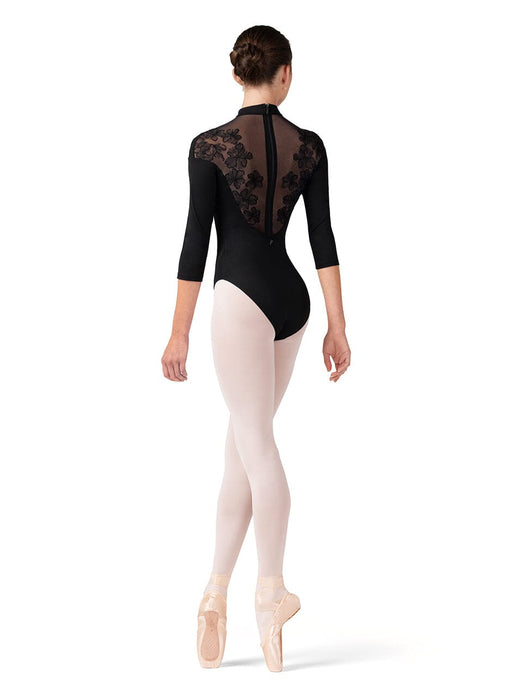 Ballerina wearing a black leotard with floral lace details and white tights on a white background