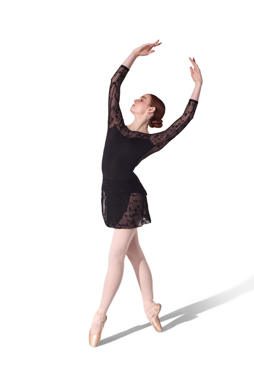 A female dancer in a black lace long-sleeve leotard and pointe shoes, posed in a classical ballet position against a solid white background.