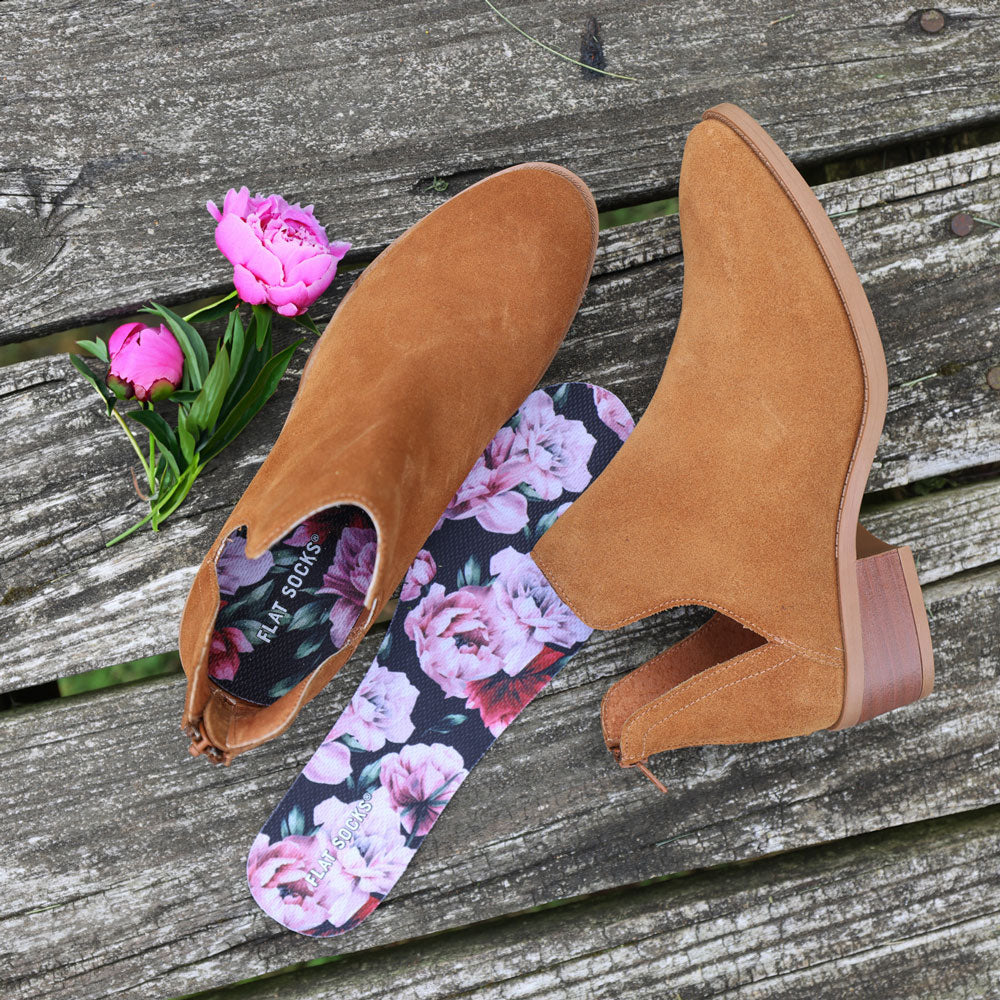 Brown suede ankle boots with floral insoles on a wooden surface with pink flowers.