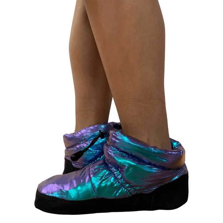 Iridescent shoe covers on a person's feet with a white background