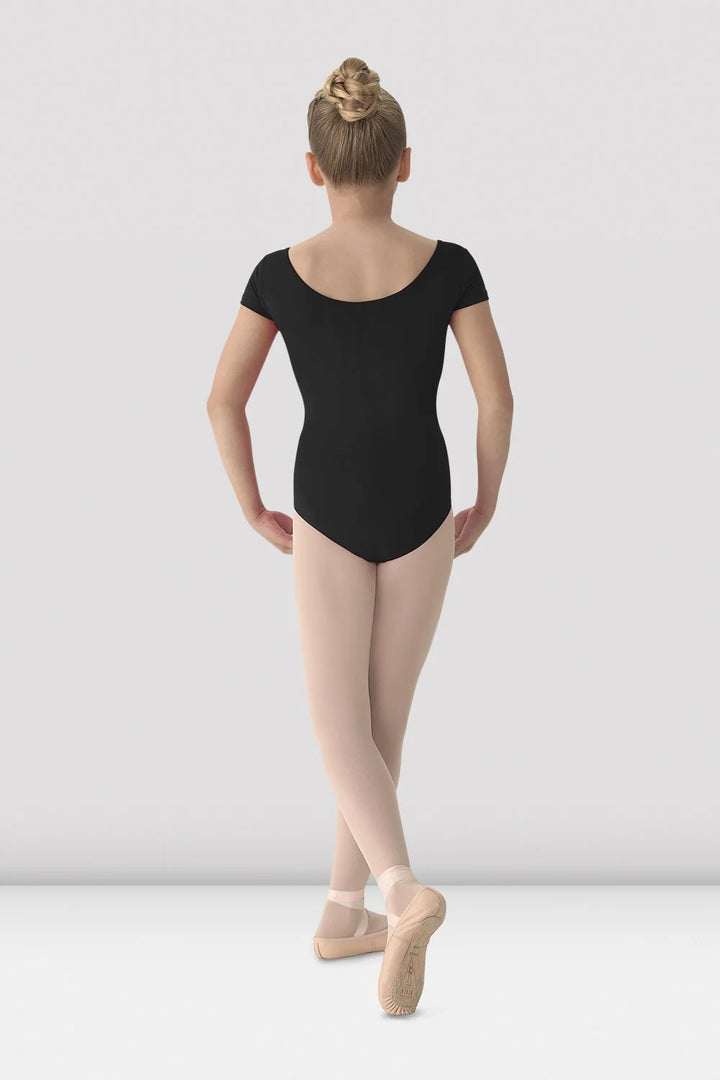 A young ballerina viewed from behind, wearing a black short-sleeve leotard, nude tights, and pink pointe shoes against a light gray studio background.