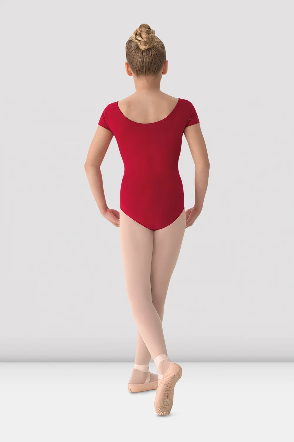 Young dancer in a red leotard and beige tights on a white background