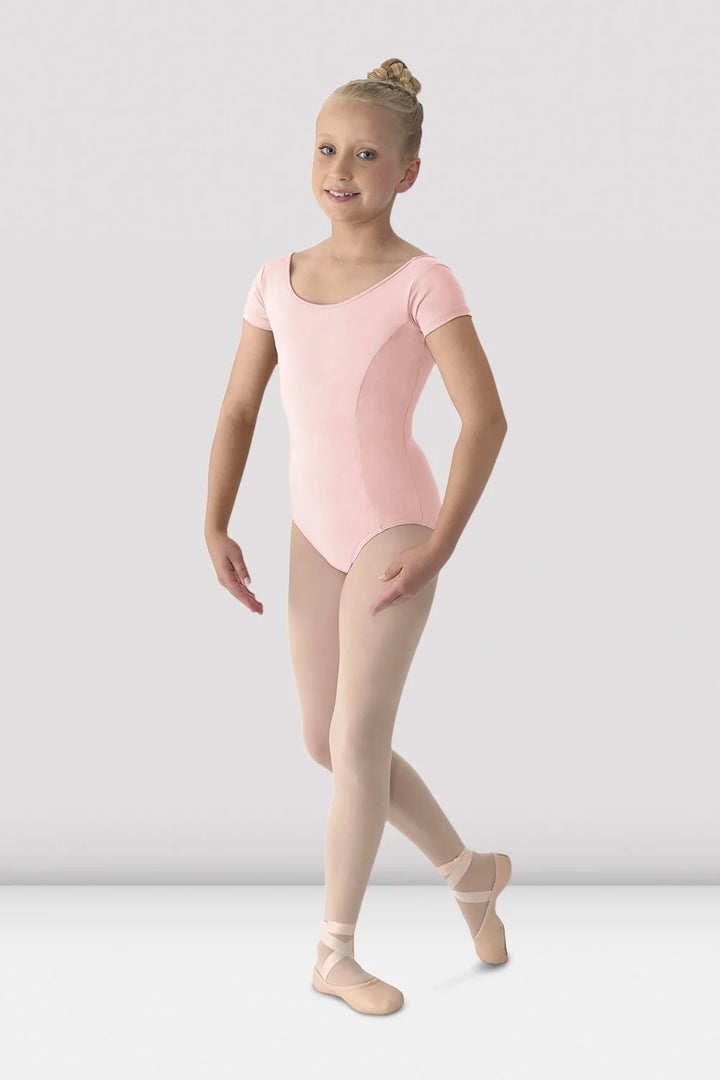 Young girl in a pink leotard and beige tights standing against a white background