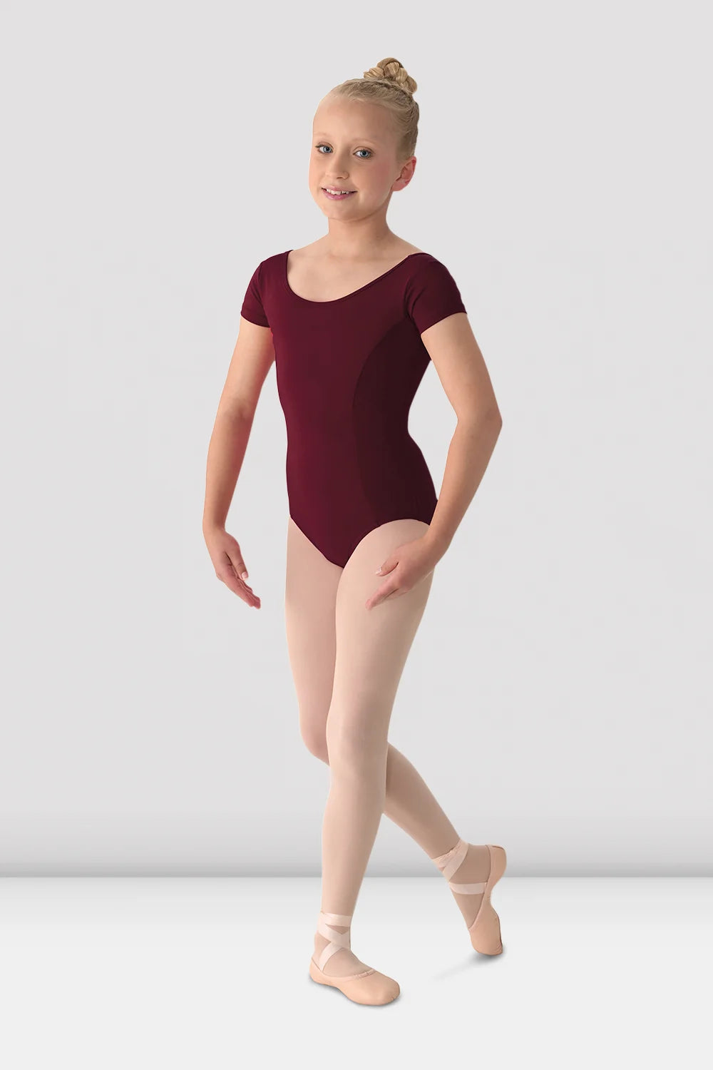 Young girl in a maroon leotard posing against a plain background