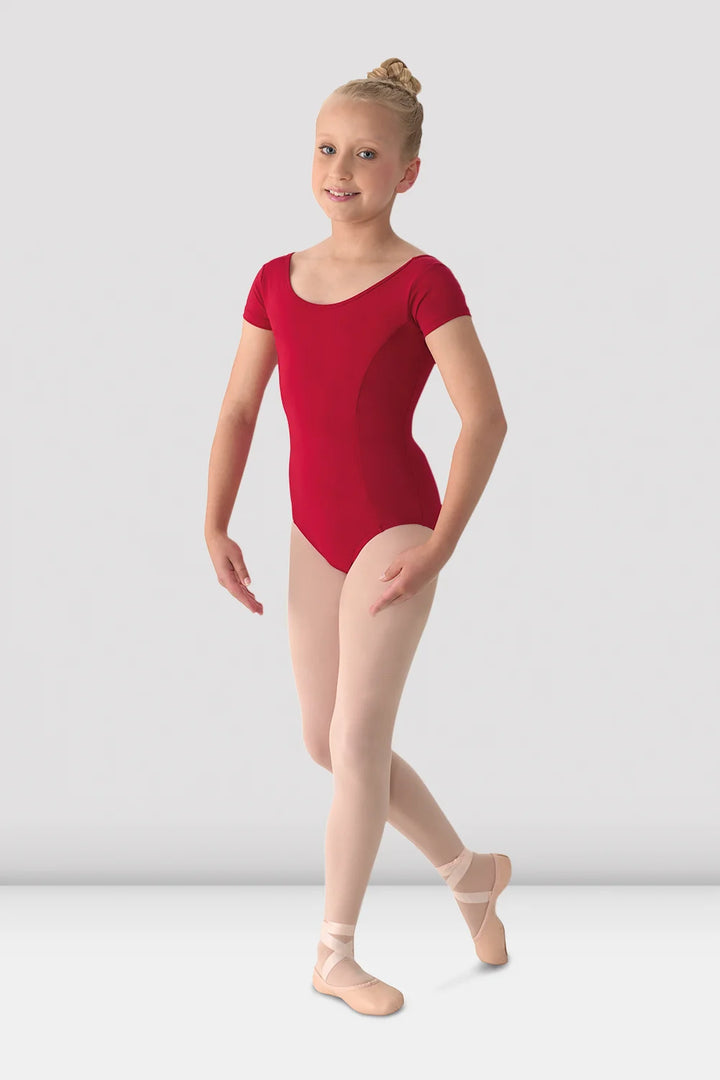A young girl dancer wearing a bright red short-sleeve leotard and light pink pointe shoes, posing against a light gray studio background.