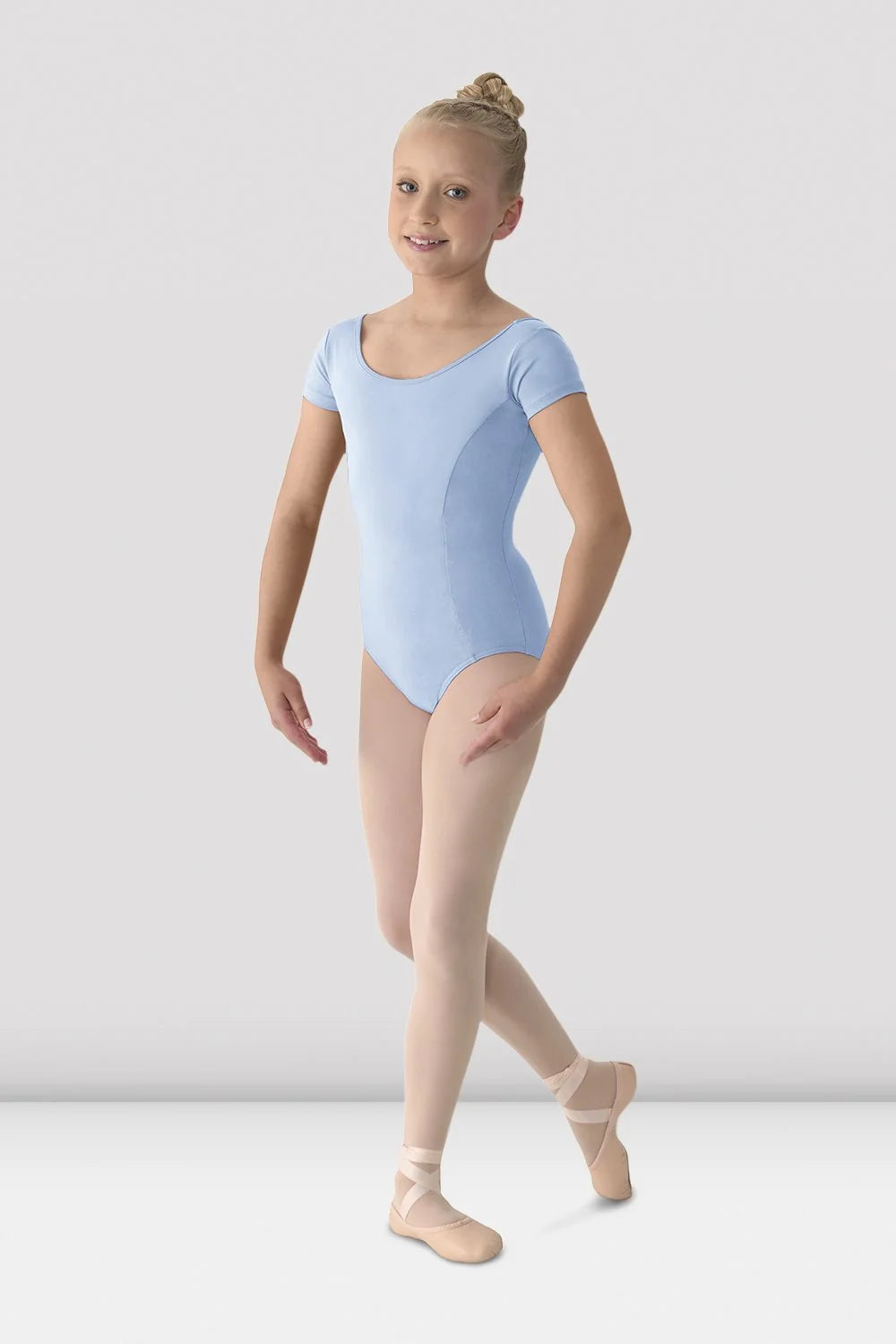 Young girl in a light blue leotard and beige tights posing against a white background
