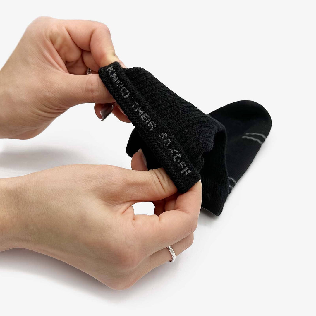 Person holding a black ankle sock with text on a white background