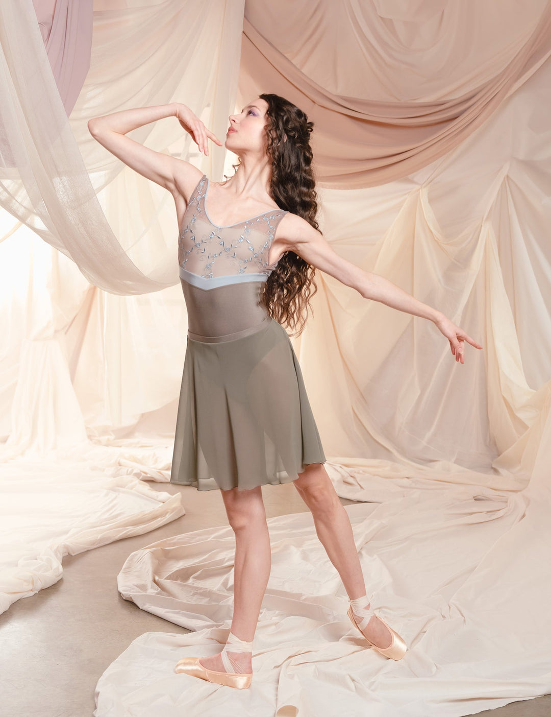 Dancer in a gray dress posing against a soft, draped curtain background