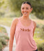 Woman wearing a pink tank top with 'Merde' printed on it, standing outdoors.