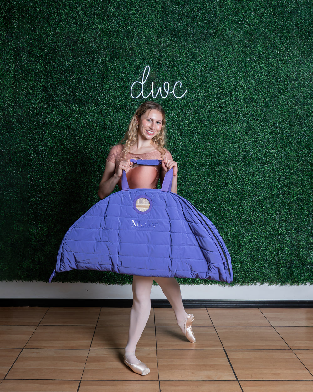 Person holding a purple dance costume against a green wall with 'divac' branding.
