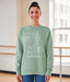 Woman wearing a light green sweatshirt with text and graphics, standing indoors.