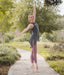 Dancer in a gray top and pink leggings posing outdoors on a path with greenery.