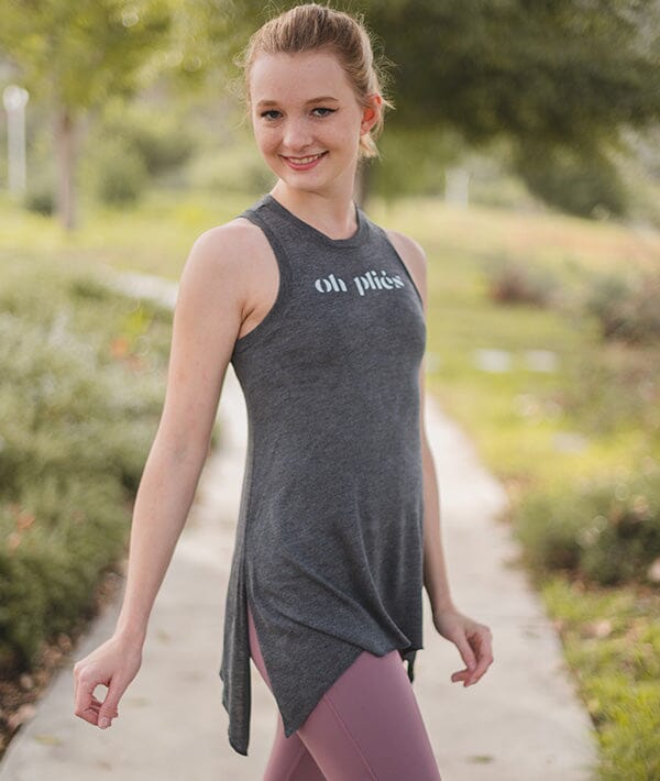 Woman wearing a dark gray sleeveless top with 'oh pls' text and pink leggings, standing outdoors.
