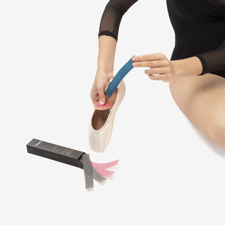 Person applying a blue shoe insert to a ballet shoe with a white background