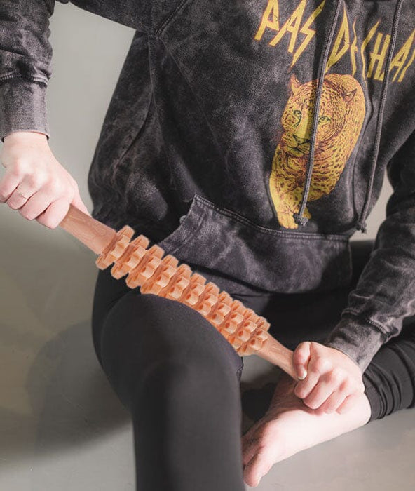 Person using a plastic massage stick on their foot, wearing a hoodie with a graphic design.