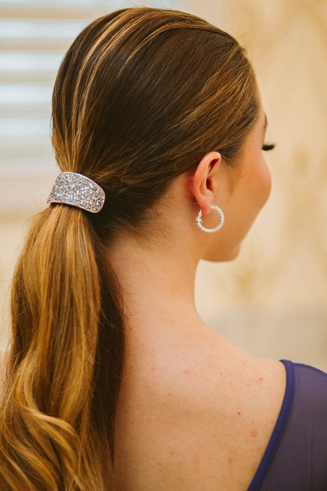 Woman with a decorative hair clip and hoop earrings, wearing a purple top.