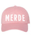Pink cap with 'MERDE' printed on it against a white background