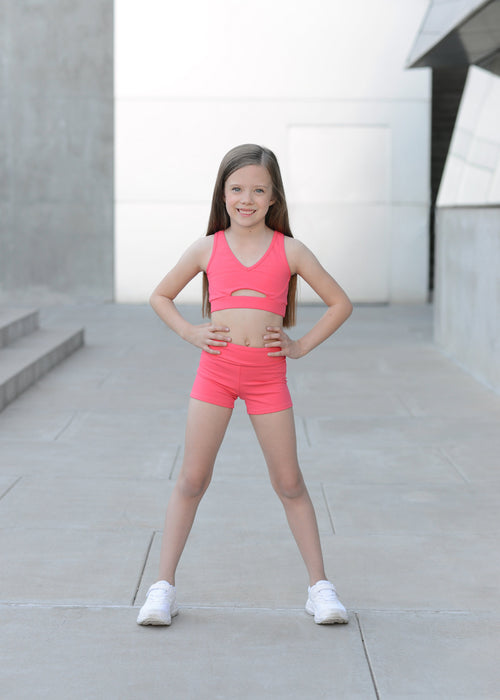Young girl in a pink athletic outfit standing on a concrete surface.