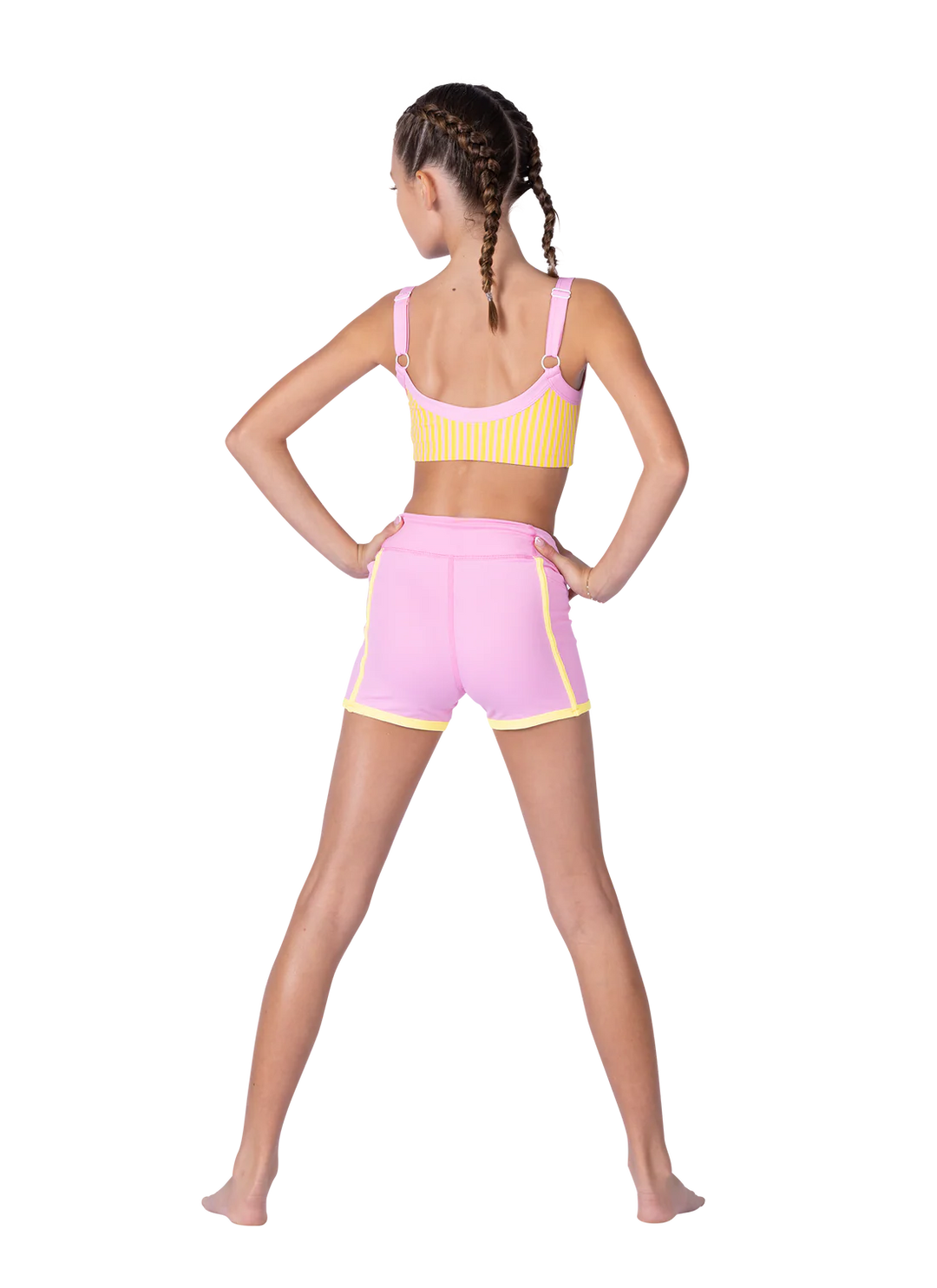 Girl wearing a yellow sports bra and pink shorts on a white background