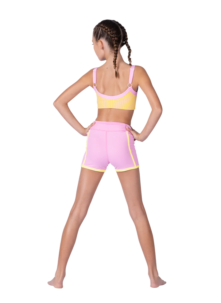 Girl wearing a yellow sports bra and pink shorts on a white background