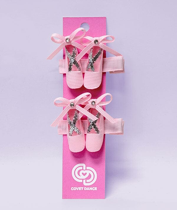 Pink ballet shoes with decorative ribbons on a pink packaging card with 'Covet Dance' logo.