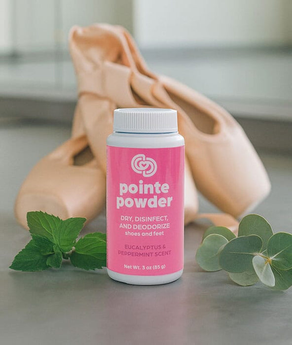 Pink bottle of pointe powder with ballet shoes and eucalyptus leaves on a neutral background