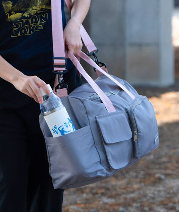 Person holding a gray duffel bag with pink straps, containing a water bottle.