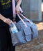 Person holding a gray duffel bag with pink straps, containing a water bottle.